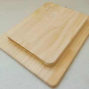 Könnte beinhalten: Zwei Holzschneidebretter, eines auf dem anderen. Das obere Brett ist etwas größer und hat abgerundete Kanten. Beide Bretter sind aus hellem Holz.