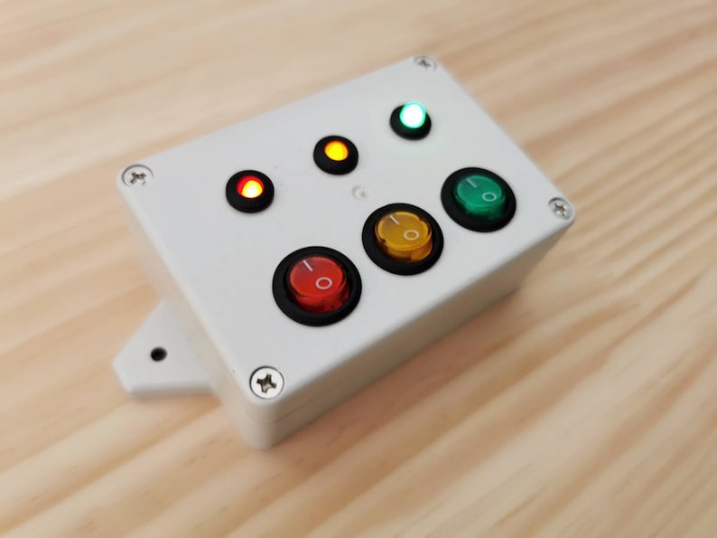 A white box with four toggle switches and four indicator lights. The lights are red, yellow, green, and white. The switches are black with red, yellow, green, and white buttons.