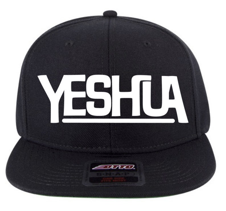 May include: Black and white snap back baseball cap with the word "YESHUA" in white letters on the front.