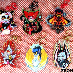 Peut inclure: Six porte-clés en acrylique avec des personnages de dessins animés colorés. Chaque porte-clés présente un design unique avec des couleurs vives, notamment du rouge, du jaune, du noir et du blanc. Les porte-clés sont attachés à des fermoirs rouges ou dorés.