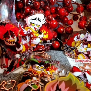 Puede incluir: Un conjunto de cuatro dijes de acrílico con temática navideña que representan personajes de dibujos animados. Los dijes son rojos, blancos y amarillos con contornos negros. Los personajes son un demonio rojo con cuernos, un ángel blanco con alas, un personaje amarillo con una corona y un personaje rojo con una corona. Los dijes tienen texto que dice "I can pull you to hell for you, steam", "Original Stocking Stuffer", "Naughty or Nice?" y "SunnyCitrineCrafts".
