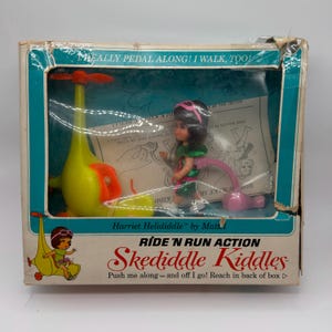 May include: A vintage Harriet Helididdle Skediddle Kiddles toy by Mattel in its original box. The set includes a small doll with dark hair and a green outfit, a yellow helicopter-style walker with orange rotors, and a pink attachment piece.