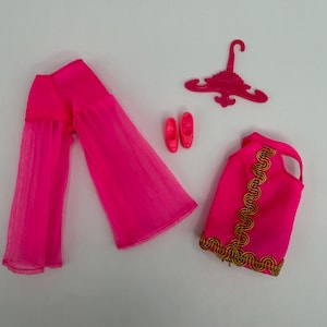 May include: A set of doll clothing including bright pink wide-leg trousers with sheer fabric overlays, a sleeveless bright pink top with gold braided trim along the front and hem, a pair of bright pink flat shoes, and a bright pink plastic hanger.