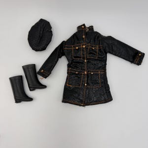 May include: A black doll-sized outfit, including a jacket, hat, and boots. The jacket has gold-colored buttons and stitching. The boots are knee-high. The hat is a rounded shape. The outfit is on a white background.