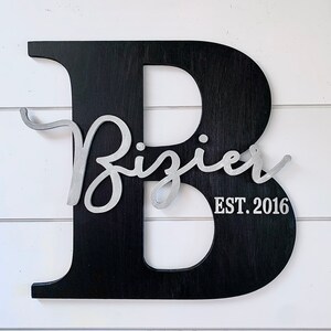 May include: Black wooden letter B with a silver cursive inscription that reads "Bizier EST. 2016".