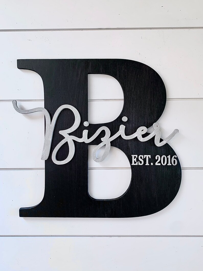 May include: Black wooden letter B with a silver cursive inscription that reads "Bizier EST. 2016".