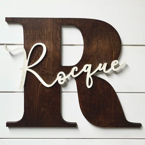 May include: A dark brown wooden letter R with the name "Roque" written in white cursive script.
