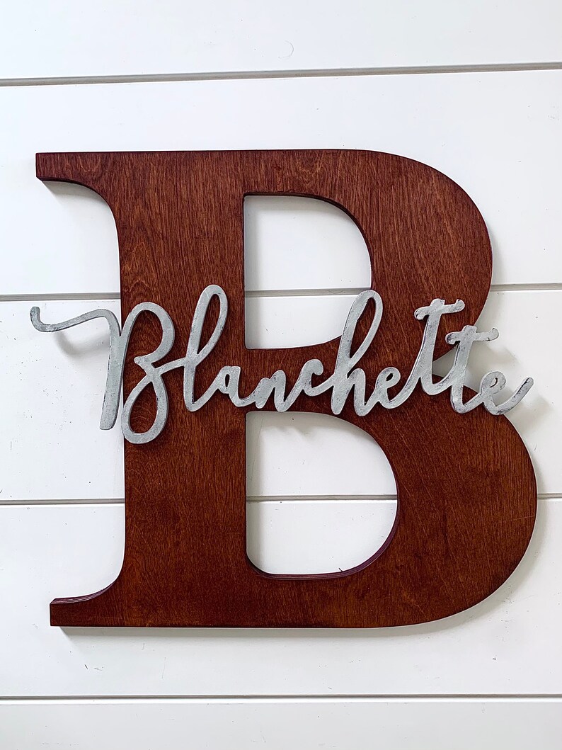 May include: A wooden letter B painted in a dark brown colour with the name "Blanchette" written in silver metal letters on the front of the letter.