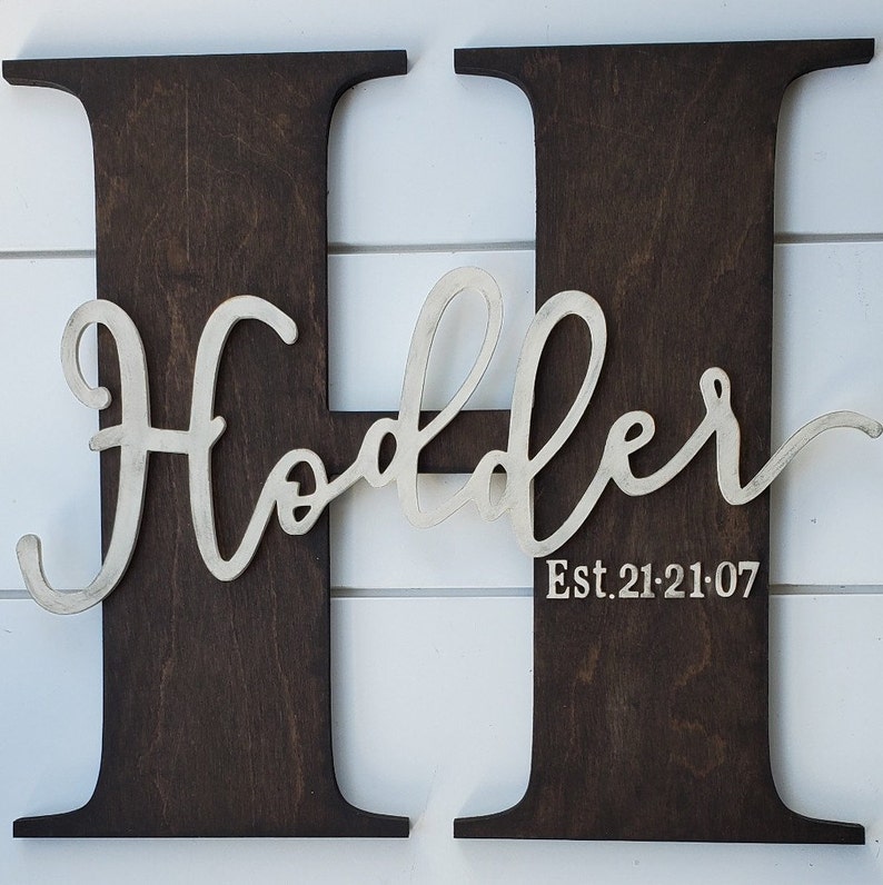 May include: A dark brown wooden letter H with the word "Holder" in white cursive lettering and the text "Est. 21.21.07" below it.