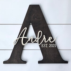 May include: A dark brown wooden letter A with the name "Andre" and the text "EST. 2021" in white lettering.