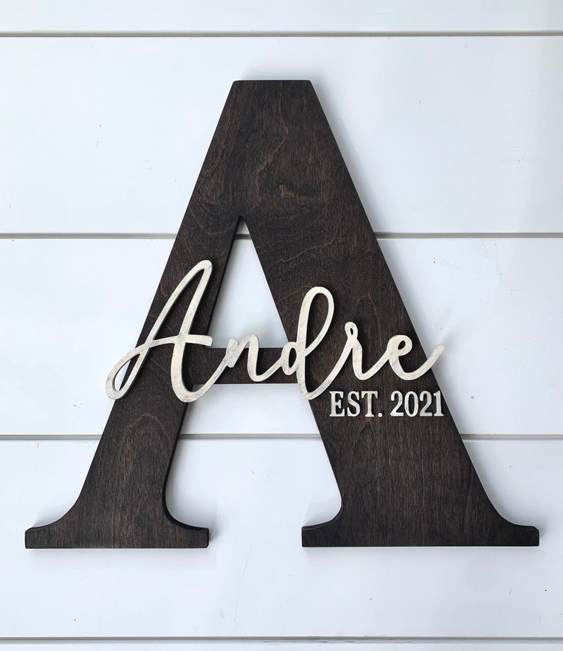 May include: A dark brown wooden letter A with the name "Andre" and the text "EST. 2021" in white lettering.
