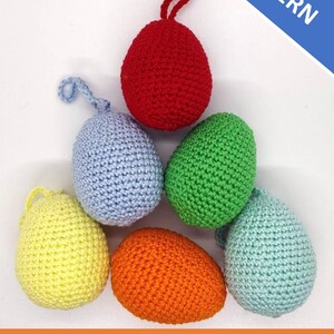 May include: Six crocheted Easter eggs in different colors: red, light blue, green, yellow, orange, and light blue. The eggs are arranged in a triangle shape. The text "PDF PATTERN" is in the upper right corner of the image. The text "EASTER EGG basic crochet pattern" is at the bottom of the image.
