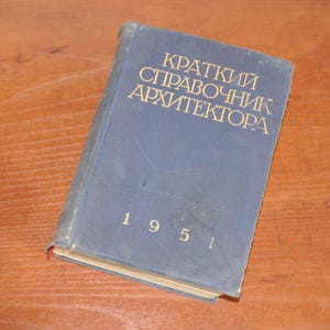 Puede incluir: Un libro de tapa dura azul con el título "Краткий справочник архитектора" y el año "1951" impreso en la portada.