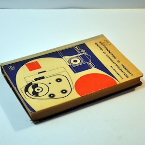 May include: A vintage book with a cover featuring a camera illustration in black and white, set against a blue and tan background with a red circle and square. The title is in Russian.