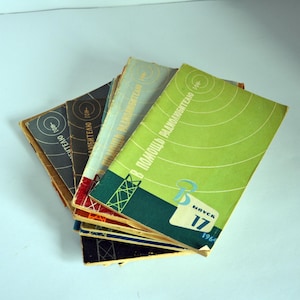 Puede incluir: Una pila de folletos antiguos con cubiertas coloridas. Las cubiertas presentan diseños geométricos y texto en un idioma extranjero. Los folletos son de varios colores, incluyendo verde, azul y gris. El año 1964 es visible en una cubierta.