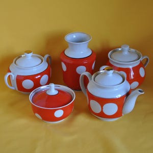 May include: A vintage tea set with a teapot, sugar bowl, creamer, and two lidded serving dishes. The set features a white and orange color scheme with large white polka dots. The teapot has a spout and handle.