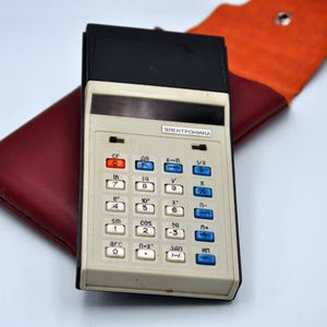 Könnte beinhalten: Ein weißer und schwarzer Vintage-Rechner mit blauen und roten Tasten. Der Rechner ist mit "ЭЛЕКТРОНИКА" beschriftet und verfügt über eine Vielzahl mathematischer Funktionen.
