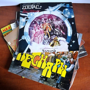 Könnte beinhalten: Ein Stapel Vintage-Schallplatten, darunter eine Schallplatte mit dem Titel "Zodiac" von "Disco Alliance", einer Instrumental-Rockgruppe. Die oberste Schallplatte zeigt eine farbenfrohe Illustration eines Raumschiffs und einer Gruppe von Menschen in futuristischer Kleidung. Die unterste Schallplatte trägt den Schriftzug "TECHNO" in gelben Buchstaben.