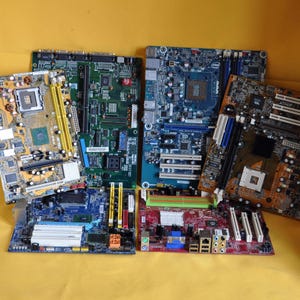 May include: A collection of computer motherboards in various colors, including green, blue, red, and gold. The motherboards are arranged on a yellow surface, showcasing their intricate electronic components and connectors. The image highlights the diversity of computer hardware.