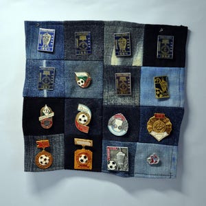 Puede incluir: Un mosaico de cuadrados de mezclilla que muestra pines y insignias de fútbol vintage. Los pines presentan balones de fútbol, trofeos y el texto "Dynamo" y varios años. Los cuadrados de mezclilla son en tonos de azul y negro.