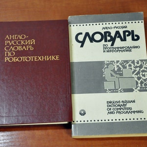 Puede incluir: Dos libros de tapa dura con cubiertas rojas y blancas. El libro de la izquierda tiene el título "DICCIONARIO INGLÉS-RUSO DE ROBÓTICA" en letras doradas. El libro de la derecha tiene el título "DICCIONARIO INGLÉS-RUSO DE COMPUTADORAS Y PROGRAMACIÓN" en letras negras.