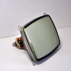 Puede incluir: Una pantalla de televisión vintage con un marco plateado y un bisel negro. La pantalla está en blanco y la televisión está montada en un soporte.