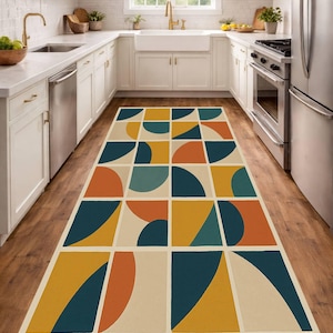 May include: A rectangular kitchen rug with a geometric pattern. The rug features squares and semi-circles in teal, orange, yellow, and cream colors. The rug is placed on a wooden floor in a kitchen setting.
