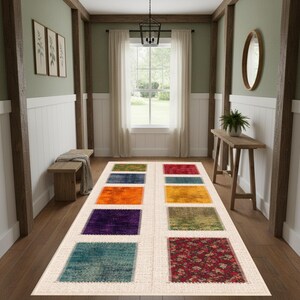 Könnte beinhalten: Ein rechteckiger Teppich mit cremefarbenem Rand und zehn bunten quadratischen Flecken. Die Flecken weisen Farbtöne von Grün, Blau, Orange, Gelb, Lila und Rot auf. Der Teppich liegt in einem Flur mit Holzbalken und einem Fenster.