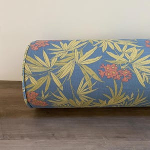 May include: A cylindrical pillow with a blue background and a repeating pattern of yellow leaves and coral-colored flowers. The pillow is made of fabric and has rounded ends. The pillow is designed for decorative or functional use.