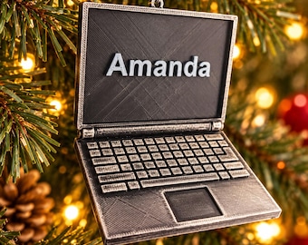 Könnte beinhalten: Ein Weihnachtsbaumschmuck in Form eines Laptops mit metallisch silbernem Finish und schwarzem Bildschirmbereich. Der Name Amanda ist in erhabenen silbernen Buchstaben auf dem Bildschirm zu sehen. Das Design umfasst eine detaillierte Tastatur.