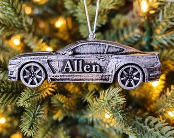 May include: A silver-toned, metallic sports car ornament featuring a weathered, brushed finish. The side of the vehicle is engraved with the name Allen in a serif font. The ornament is suspended by a thin silver string for hanging purposes.