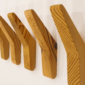 May include: Five wooden wall hooks in a light brown color, arranged in a staggered pattern. The hooks are shaped like a curved arrow pointing to the right.