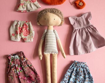 May include: A handmade doll with brown hair and a striped shirt, along with a variety of clothing items, including floral dresses, a skirt, shorts, and a hat.