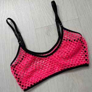 May include: A neon pink crop top with a fishnet design. The top has black trim and adjustable black straps. The garment is made of a mesh material.
