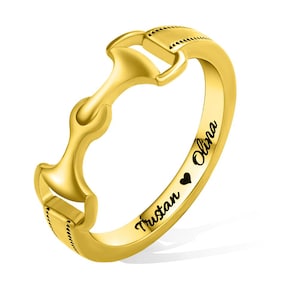 Könnte beinhalten: Goldring mit einem Pferdebiss-Design und graviert mit den Namen "Tristan" und "Olivia", die durch ein Herzsymbol getrennt sind.