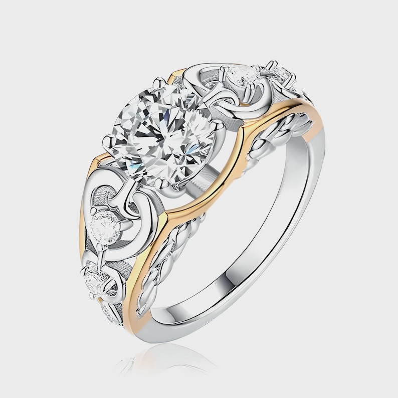 May include: A silver and gold ring with a large, clear, round-cut center stone. The ring features intricate filigree and smaller accent stones. The band has a braided design, and the ring has a two-tone color scheme.
