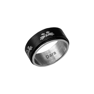 May include: A black and silver spinner ring with a cat face design. The ring has the name "Dara" engraved on the inside. The cat face design is repeated around the black band of the ring.