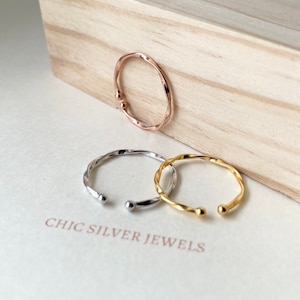 May include: Three twisted metal rings in gold, silver, and rose gold. The rings are displayed on a wooden surface with the text "Chic Silver Jewels".