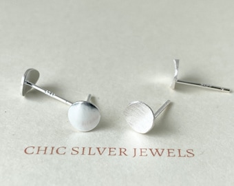 Puede incluir: Dos pendientes de botón de plata con frentes redondos y planos. Los pendientes están sobre una superficie blanca con el texto "CHIC SILVER JEWELS".