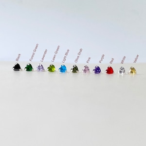 Puede incluir: Una fila de 11 piedras preciosas en forma de corazón de varios colores, incluyendo negro, verde bosque, lavanda, verde césped, azul claro, verde oliva, rosa, morado, rojo, blanco y amarillo.