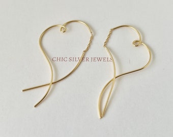 Può includere: Un paio di orecchini a forma di cuore dorati con una delicata catena che collega i due cuori. Gli orecchini sono realizzati in filo sottile e hanno un design semplice ed elegante.  "CHIC SILVER JEWELS" è stampato sullo sfondo bianco.