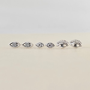 May include: Set of six silver eye earrings. The earrings feature different eye designs, including a spiral, a simple eye, and an eye with eyelashes.