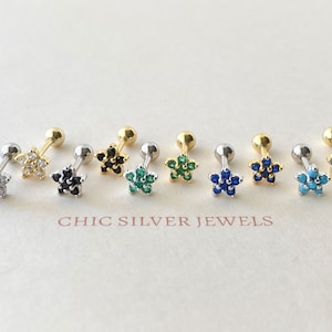 May include: Seven different flower-shaped stud earrings with gold posts and a variety of colored gemstones. The gemstones are clear, black, green, blue, and turquoise.