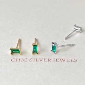 Può includere: Orecchini a bottone rettangolari verde smeraldo. Due paia sono dorati e due argentati. Gli orecchini sono esposti su una superficie bianca con il testo marrone "CHIC SILVER JEWELS".