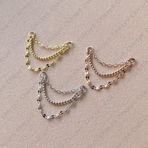 May include: Three delicate chain earrings in gold, silver, and rose gold. Each earring features three strands of varying chain styles, including beaded and flat disc designs. The earrings have a small loop at the top for easy attachment.