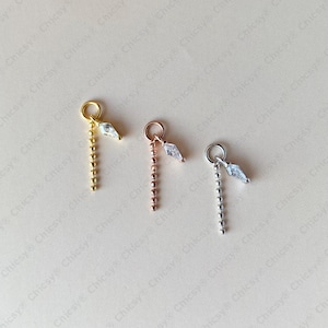 Könnte beinhalten: Drei Schmuckanhänger in Gold-, Roségold- und Silbertönen. Jeder Anhänger besteht aus einem runden Biegering, einem vertikalen Perlenkettensegment und einem kleinen, klaren, rautenförmigen facettierten Kristallstein am oberen Ring.