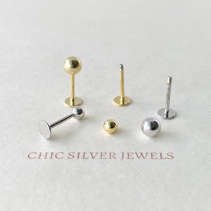 May include: Five different types of body jewellery, including a gold barbell with a ball on each end, a silver barbell with a ball on each end, and three silver studs with balls on the end. The jewellery is arranged on a white surface with the text "CHIC SILVER JEWELS" printed below.