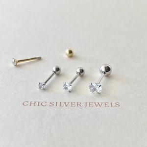 May include: Three silver barbell earrings with clear cubic zirconia stones and a gold ball earring. The earrings are on a white background with the text "CHIC SILVER JEWELS".