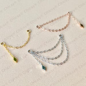 Puede incluir: Tres delicadas piezas de joyería de cadena en oro, oro rosa y plata. Cada una presenta un pequeño dije en forma de diamante. La cadena de oro es de una sola hebra, mientras que la plateada tiene tres hebras en cascada. La cadena de oro rosa es de una sola hebra.