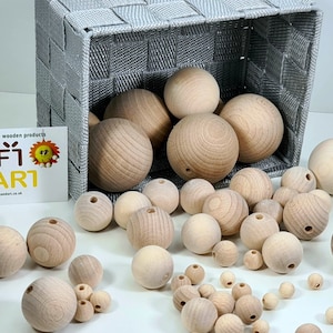 Könnte beinhalten: Eine große Auswahl an Naturholzkugeln in verschiedenen Größen, einige in einem grauen geflochtenen Korb. Die Perlen sind glatt und haben ein Loch in der Mitte. Die Perlen sind perfekt zum Basteln, Schmuckmachen und für andere DIY-Projekte.